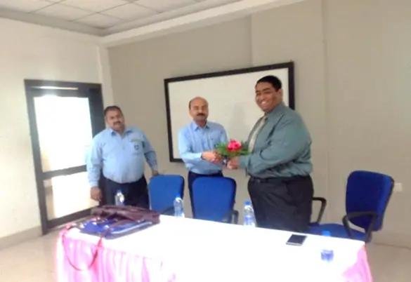 Three men in a conference room as one presents a flower bouquet during a formal meeting