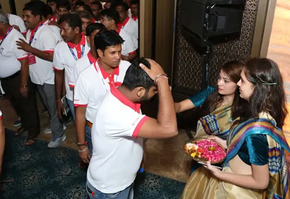 Employees receiving a traditional welcome with tilak and flowers during a company event