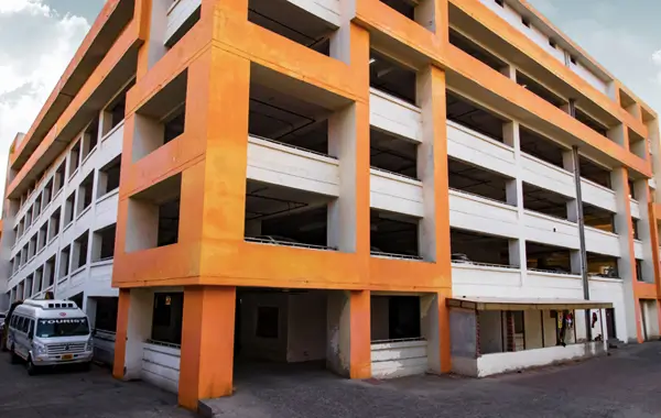 Multi-level concrete parking structure with orange and white exterior, adjacent to a tourist bus