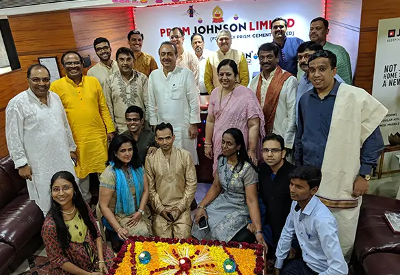 Prism Johnson employees gathered for a Diwali celebration in the office, posing around a decorative rangoli