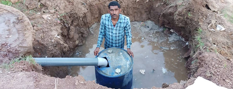Man installing a water filtration system in a dug-out pit with a barrel and pipeline for water purification